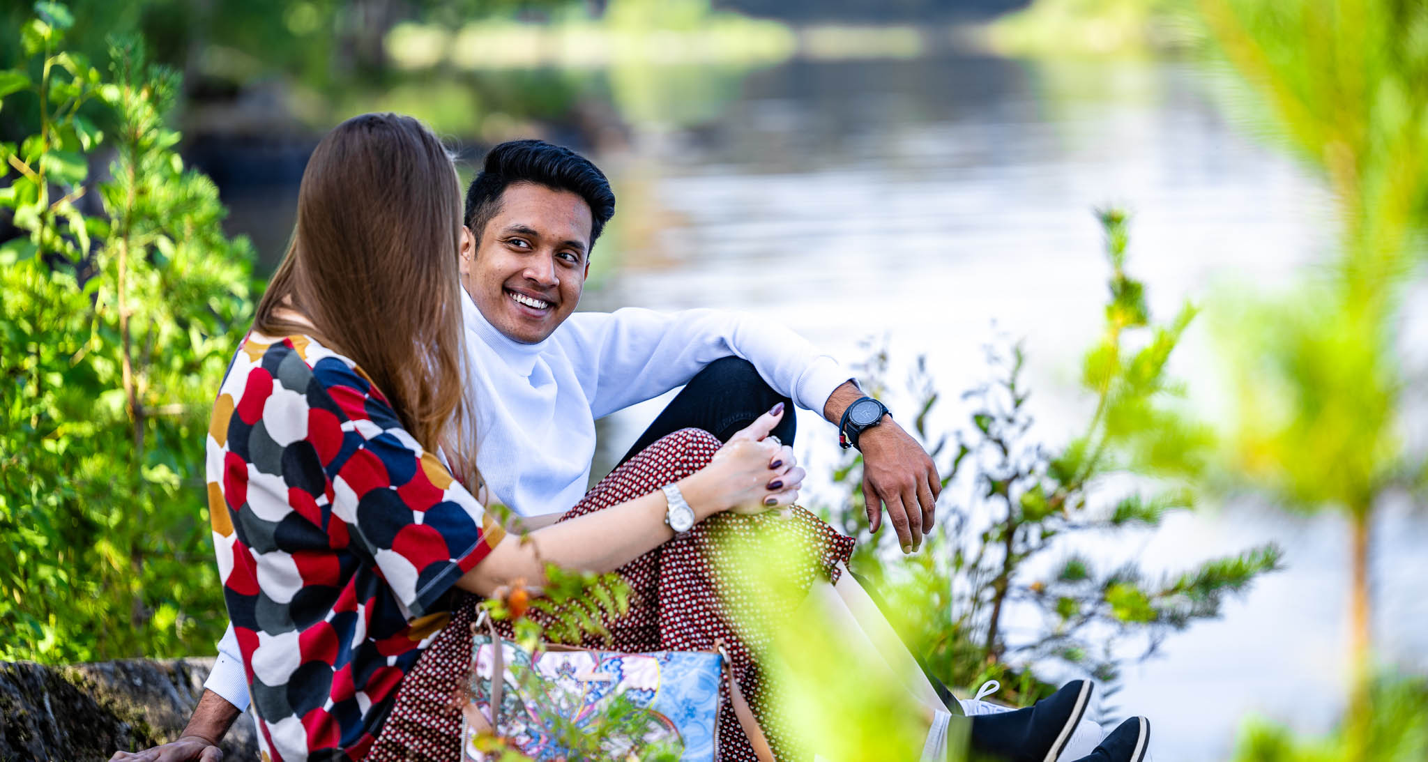 A man and a woman sit by a lake.